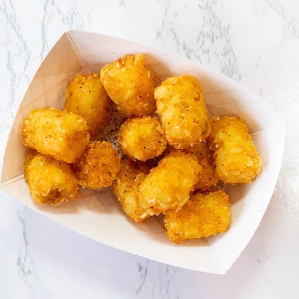 A white paper tray filled with golden brown, seasoned tater tots on a marble surface.
