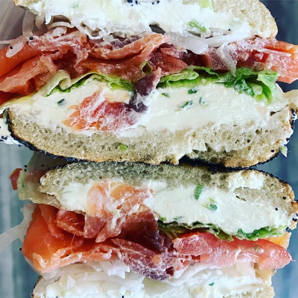 A Raceway Bagels lox and cream cheese bagel sandwich, sliced in half, revealing layers of ingredients.