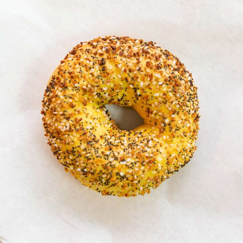 A golden-brown everything bagel from Raceway Bagels, topped with poppy seeds, sesame seeds, and garlic.