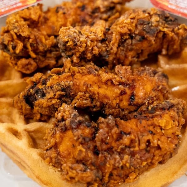 Crispy fried chicken pieces with dark seasoning resting on a golden waffle.