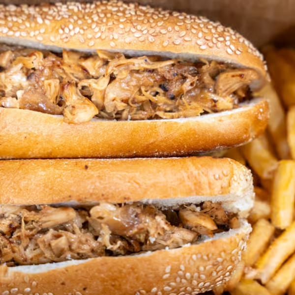 Two Raceway Bagels sandwiches filled with pulled chicken and caramelized onions, with fries in the background.