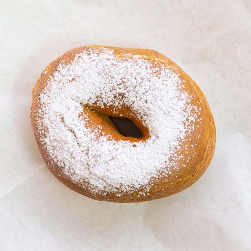 A golden-brown Raceway Bagels cinnamon sugar bagel, generously dusted with white powdered sugar.