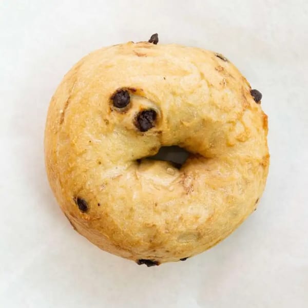 A golden-brown Raceway Bagels chocolate chip bagel with a chewy texture on a white surface.