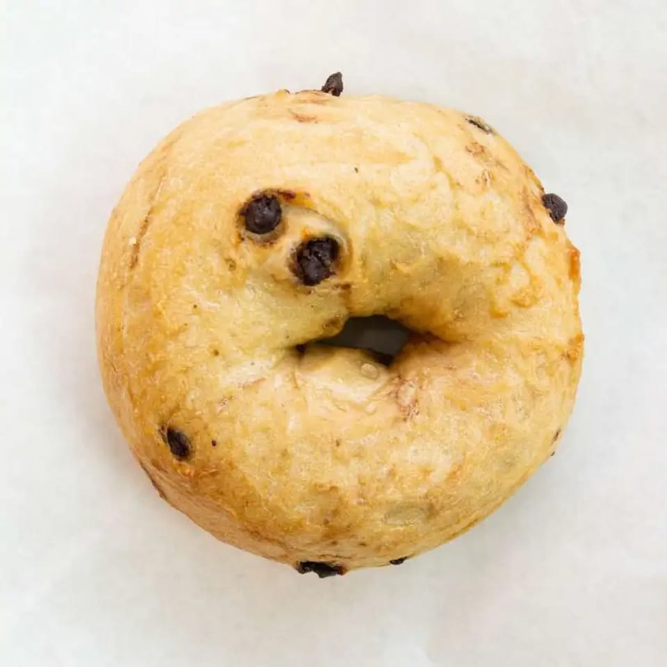 A golden-brown Raceway Bagels chocolate chip bagel with a chewy texture on a white surface.