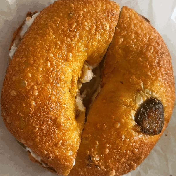 Golden-brown Raceway Bagel, sliced in half with cream cheese filling, and a dark raisin visible.