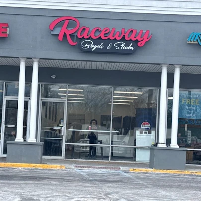 Exterior of Raceway Bagels & Steaks, a storefront with a pink sign and large windows.